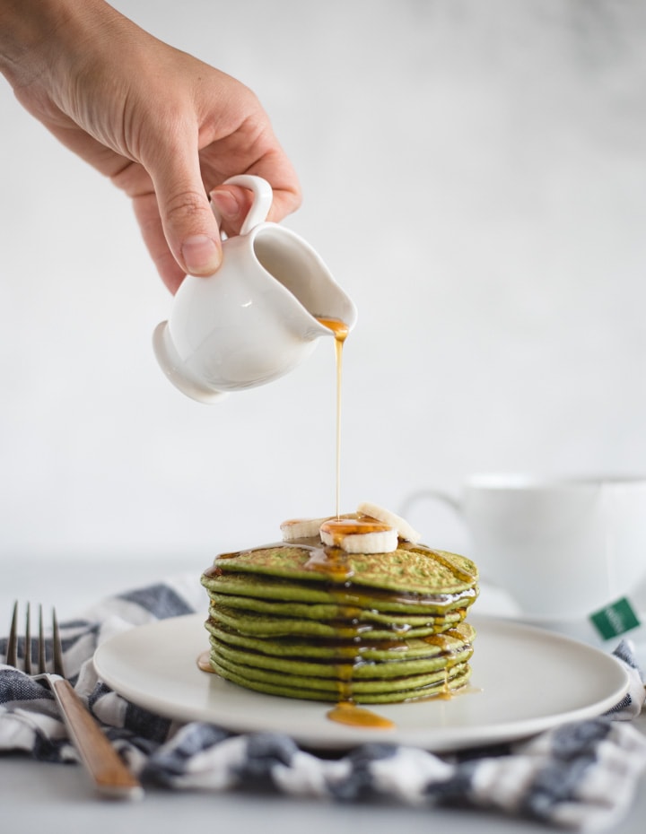 Hand pouring syrup onto a stack of spinach pancakes