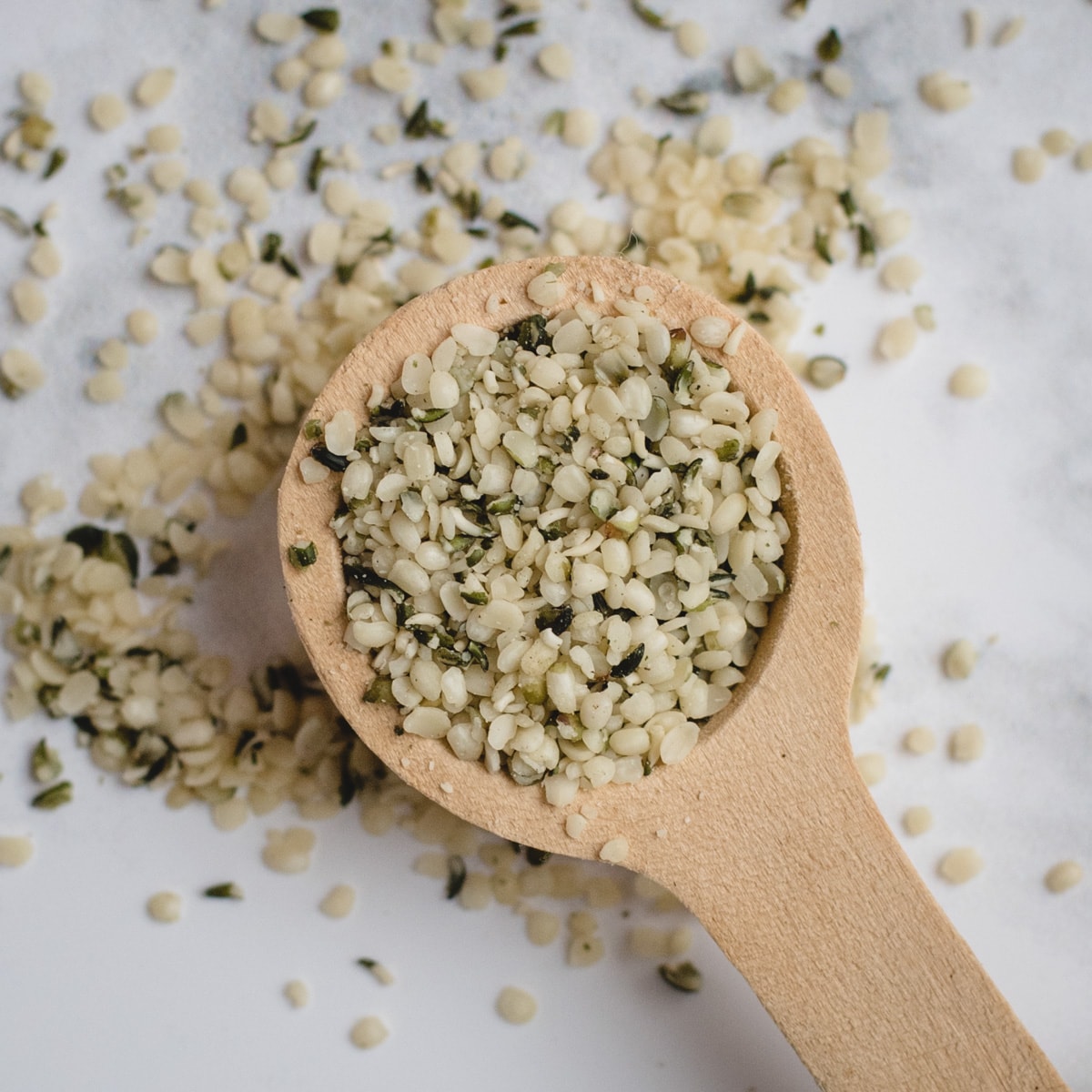 close up picture of wooden spoon with hemp hearts on white background