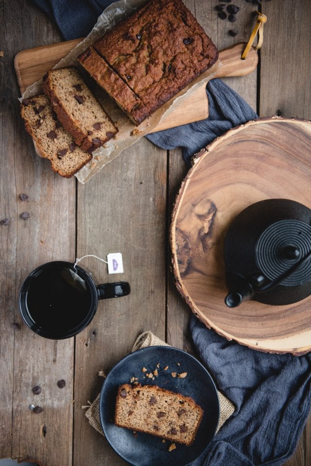 overhead picture of almond flour banana bread loaf with teapot, cup, and plate with slice of bread