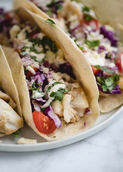 very close up picture of fish tacos on a white plate