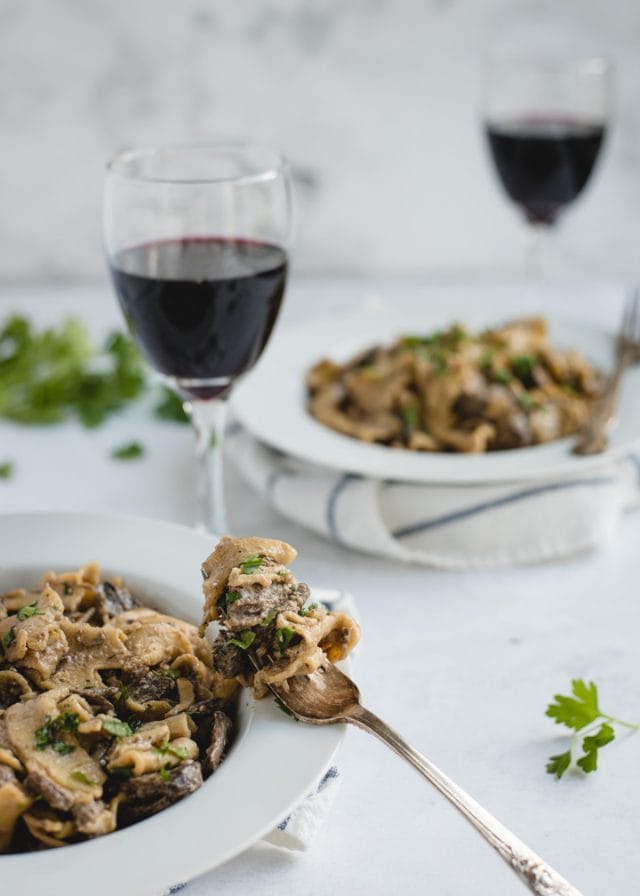 bowl of beef stroganoff with bite on fork resting on plate