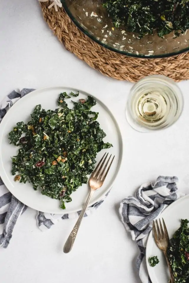 close up picture of white plate with kale salad and white wine
