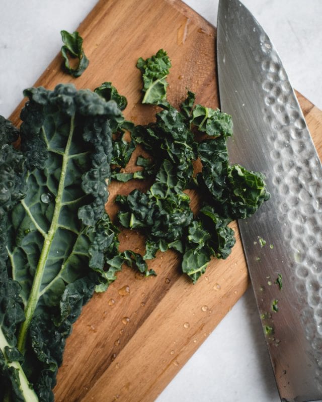 kale leaf next to chopped pieces of kale and knife on cutting board