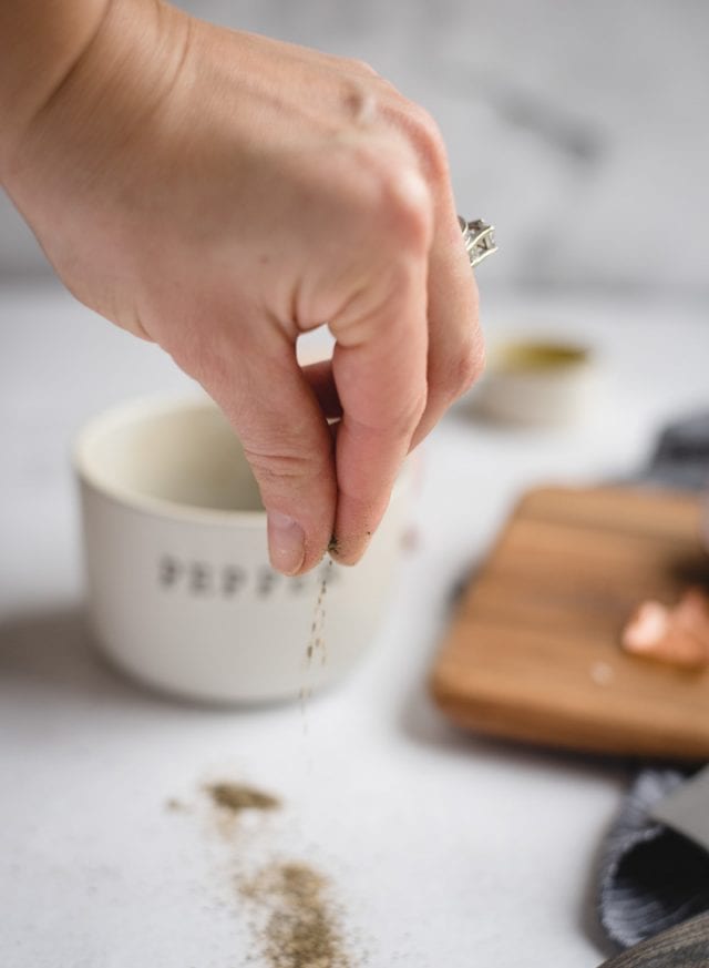 hand sprinkling black pepper with white background