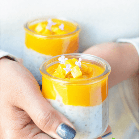 hands holding two servings of tapioca pudding with mango