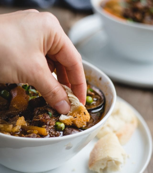 hand dipping a piece of bread in bowl of beef stew