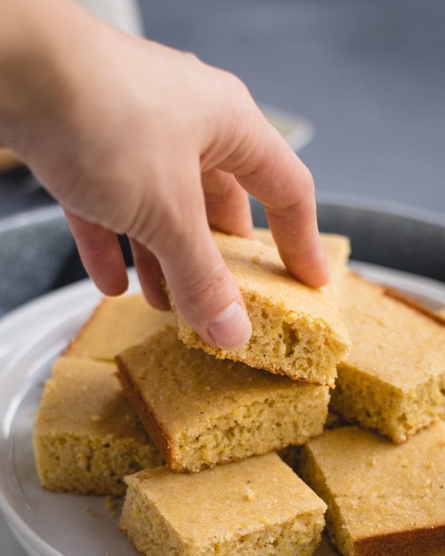 Hand grabbing a piece of cornbread from a stack 