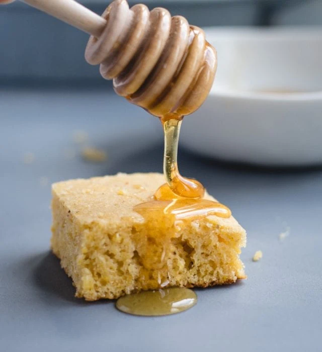 honey dipper drizzling honey on top of a square of cornbread