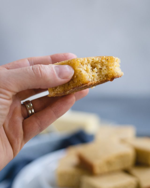 up close picture of a hand holding a piece of cornbread with a bite taken out and honey dripping off 
