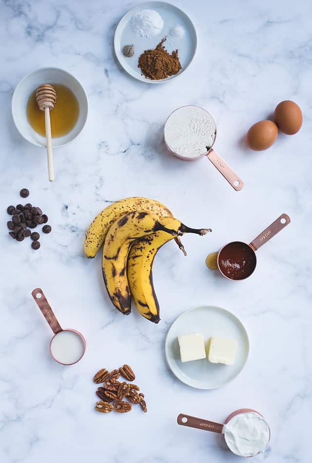 overhead picture of banana bundt cake ingredients on a white background (bananas, flour, honey, etc.)