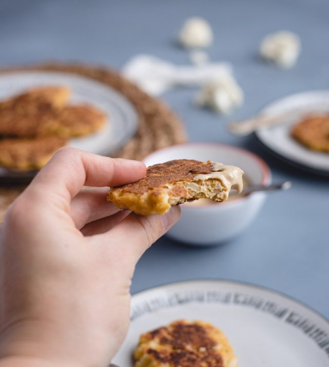 Hand holding up a cauliflower patty with a bite taken out of it