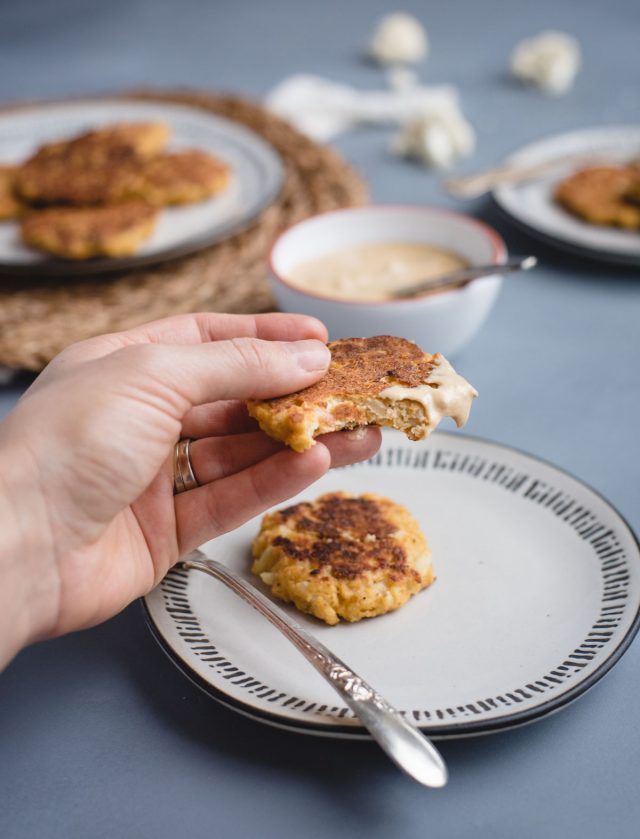 Hand holding a cauliflower patty with dipping sauce on it and a bite taken out