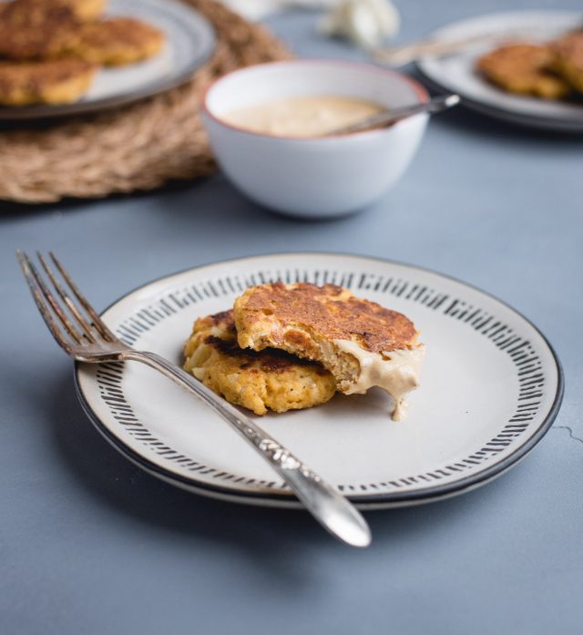 two cauliflower patties on a plate with a bite taken out of the top one