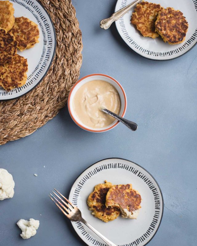 overhead picture of three plates with cauliflower patties on them on a blue background