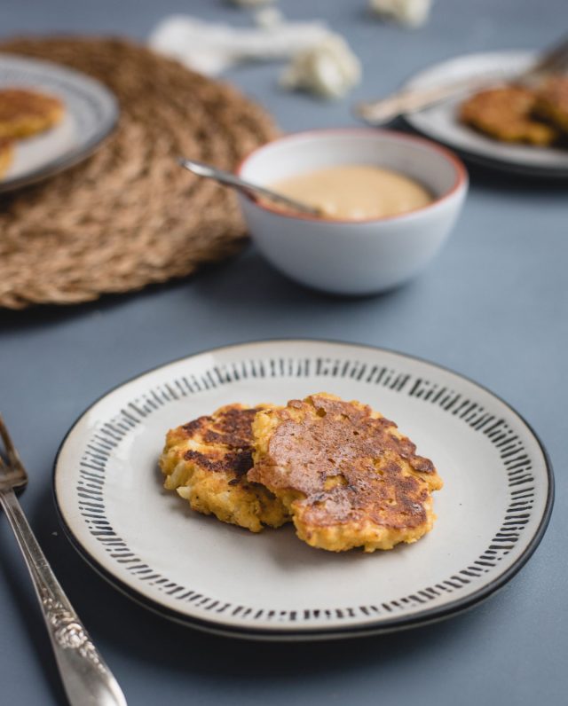 white plate with two cauliflower fritters on a blue background