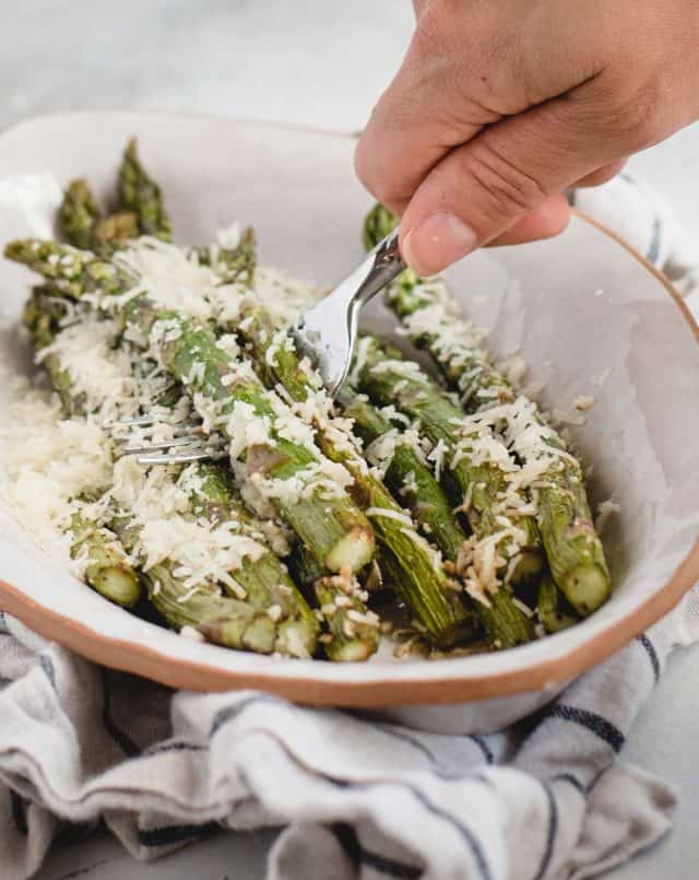 hand scooping parmesan covered asparagus spears off of a white plate