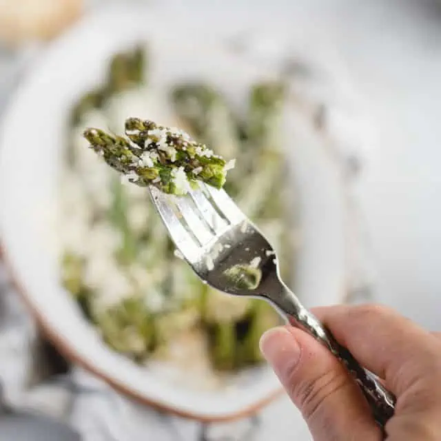 Hand holding a fork with asparagus on it against a light background