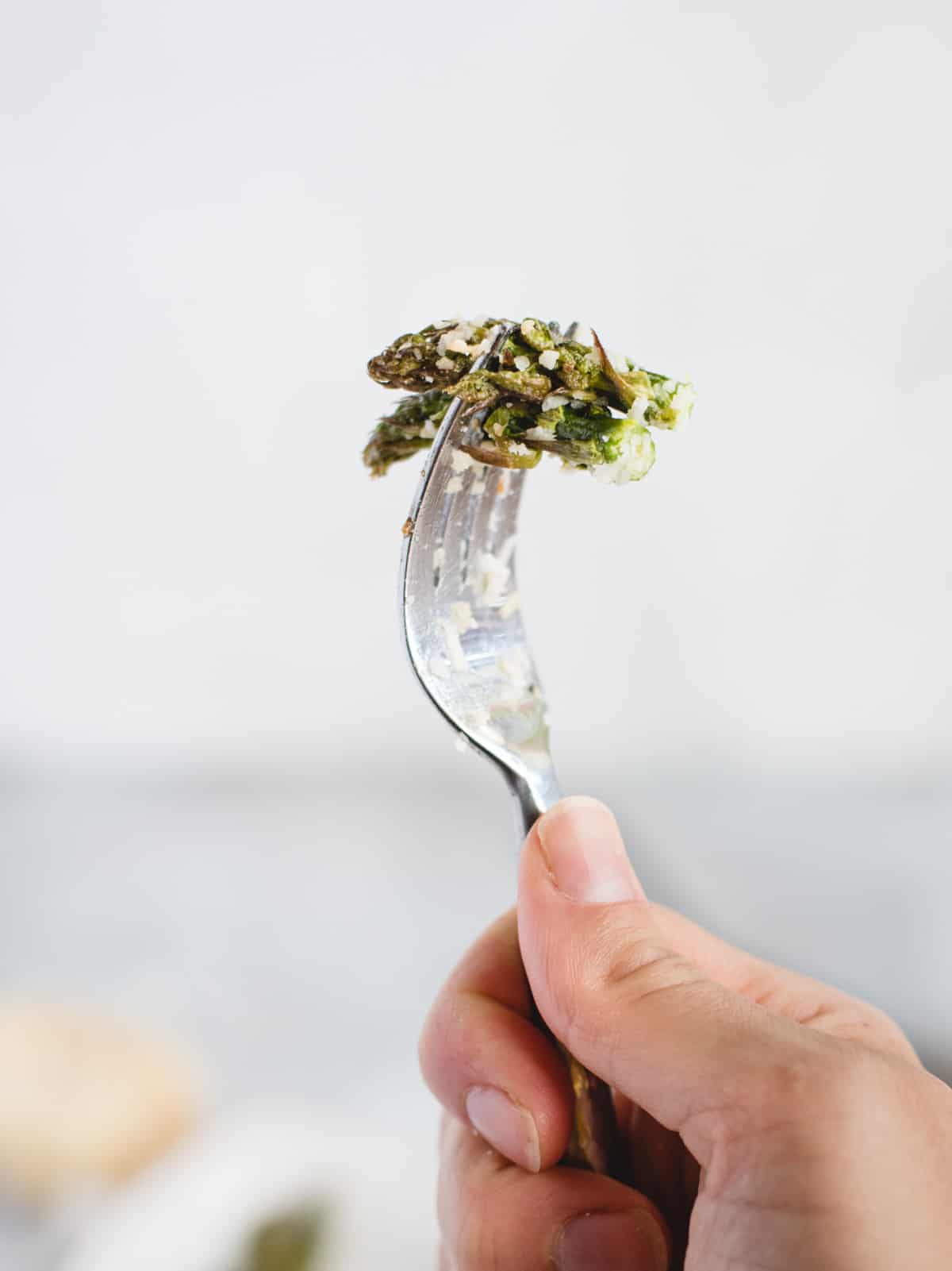 Hand holding a bit of asparagus up on a fork against a light colored background