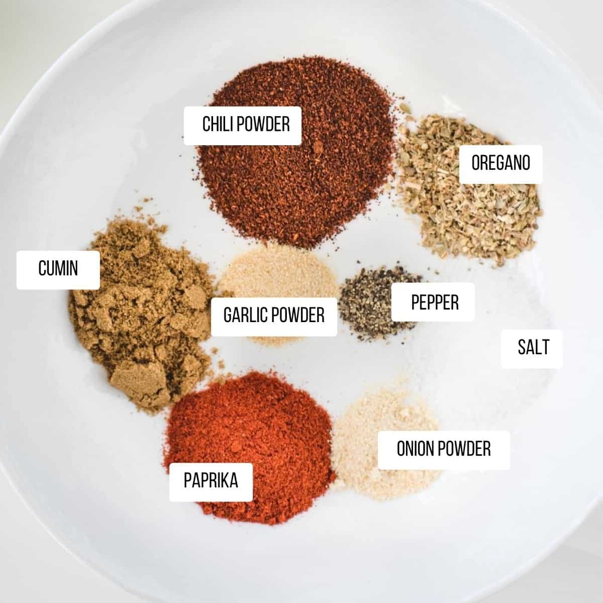 Labeled ground spices in a white bowl.