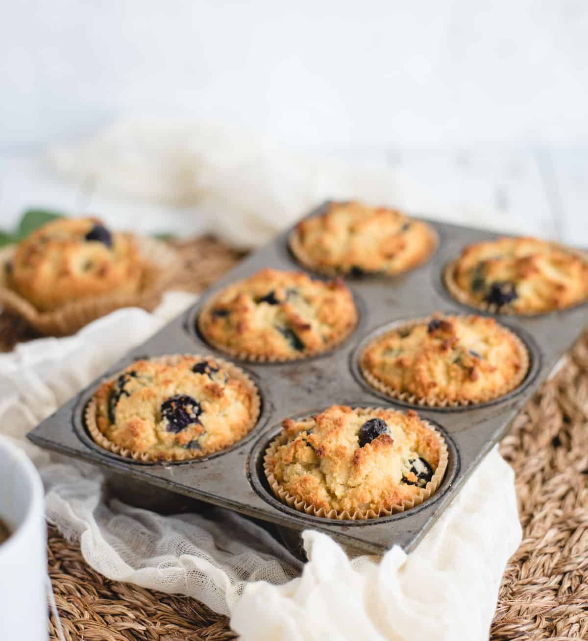 Six freshly baked muffins in a baking tin on a white backdrop
