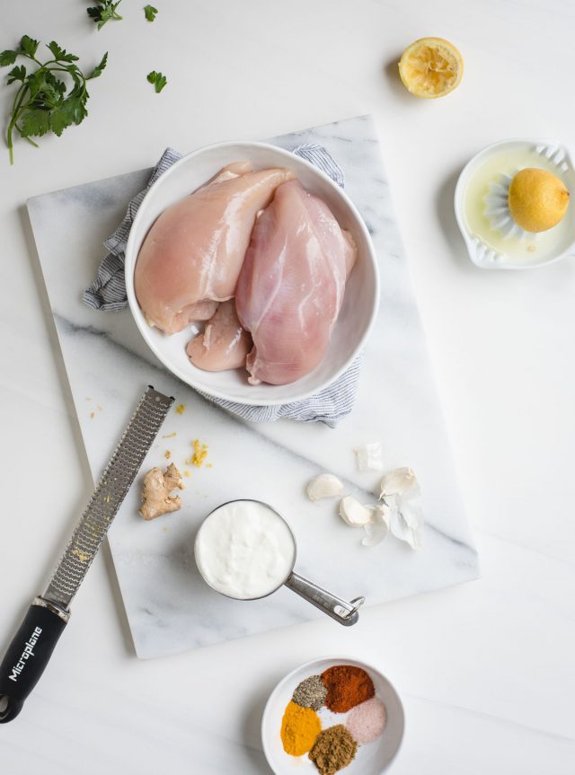 picture of chicken breasts, lemons, parsley, garlic, yogurt and spices on a white background