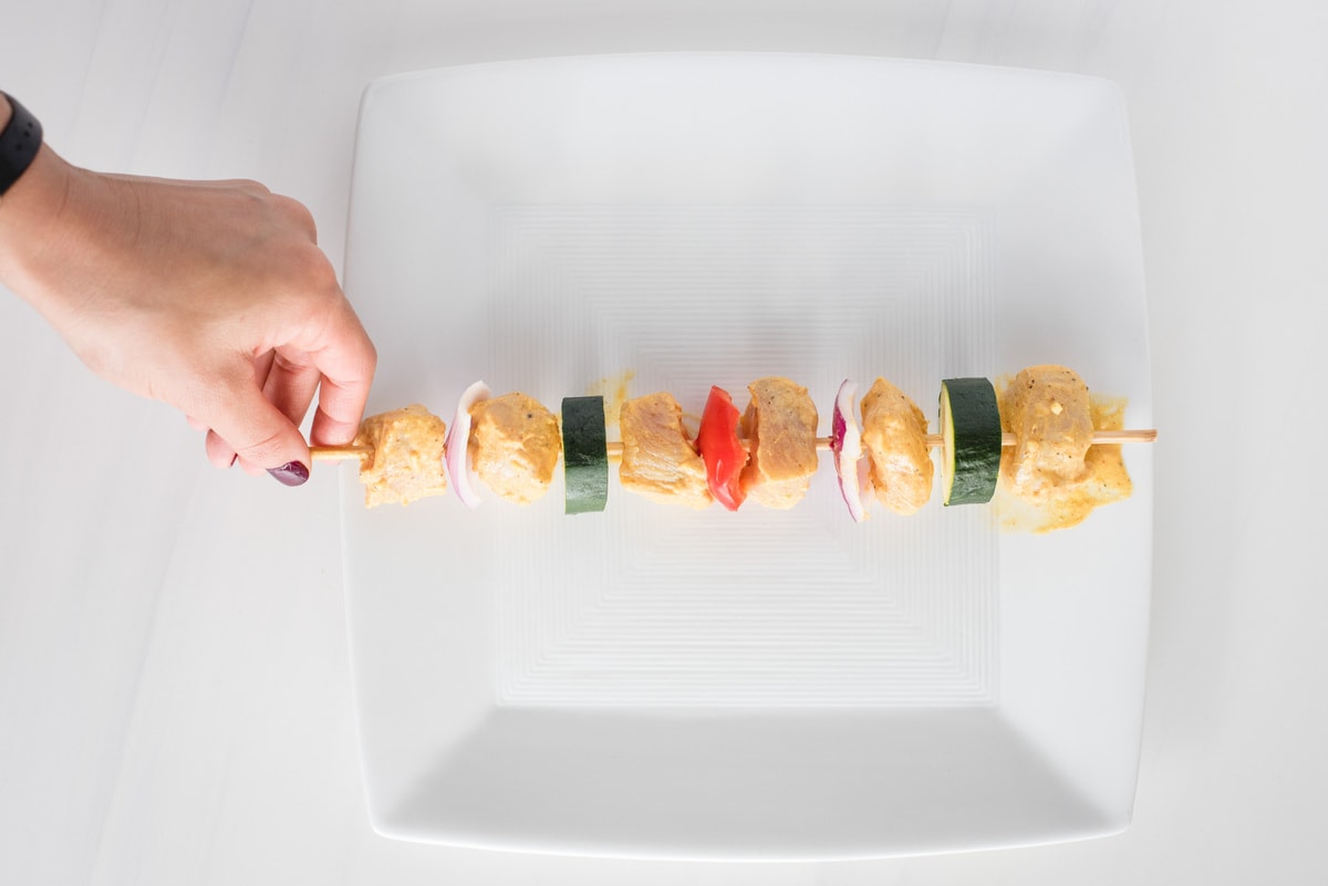  hand holding assembled chicken and veggie kabob, uncooked