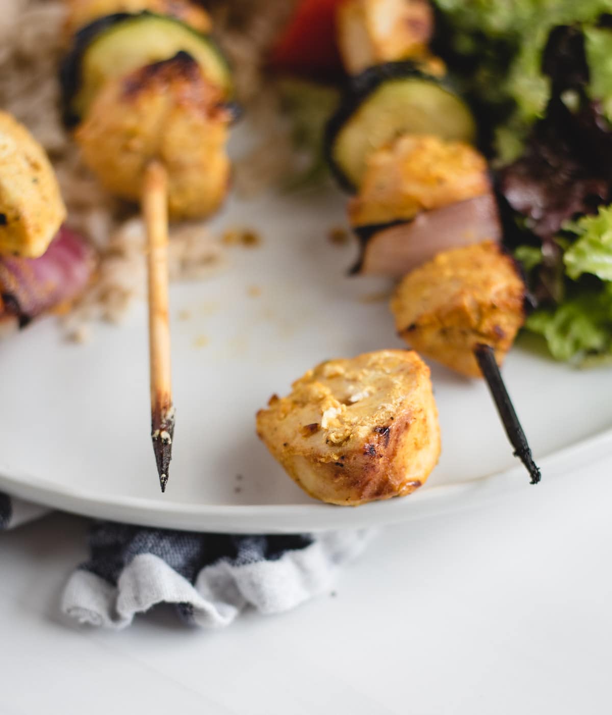 Piece of cooked chicken with kabobs in background