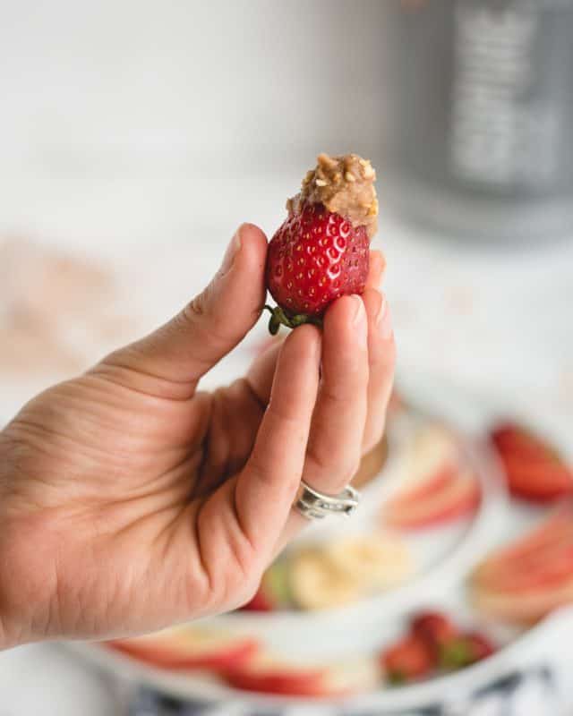 Hand holding strawberry up with chocolate hummus and peanuts on it