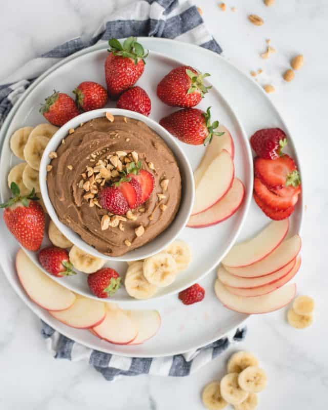 overhead picture of bowl of chocolate hummus with strawberries on white background