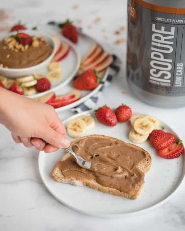 portrait photo of hand spreading chocolate hummus over a piece of toast