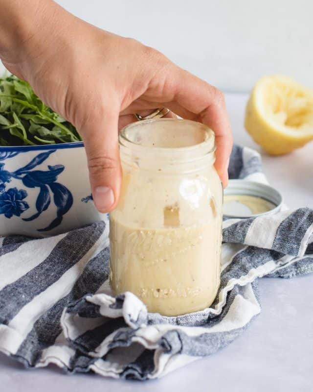 hand holding Mason jar with lemon dressing on a blue and white towel