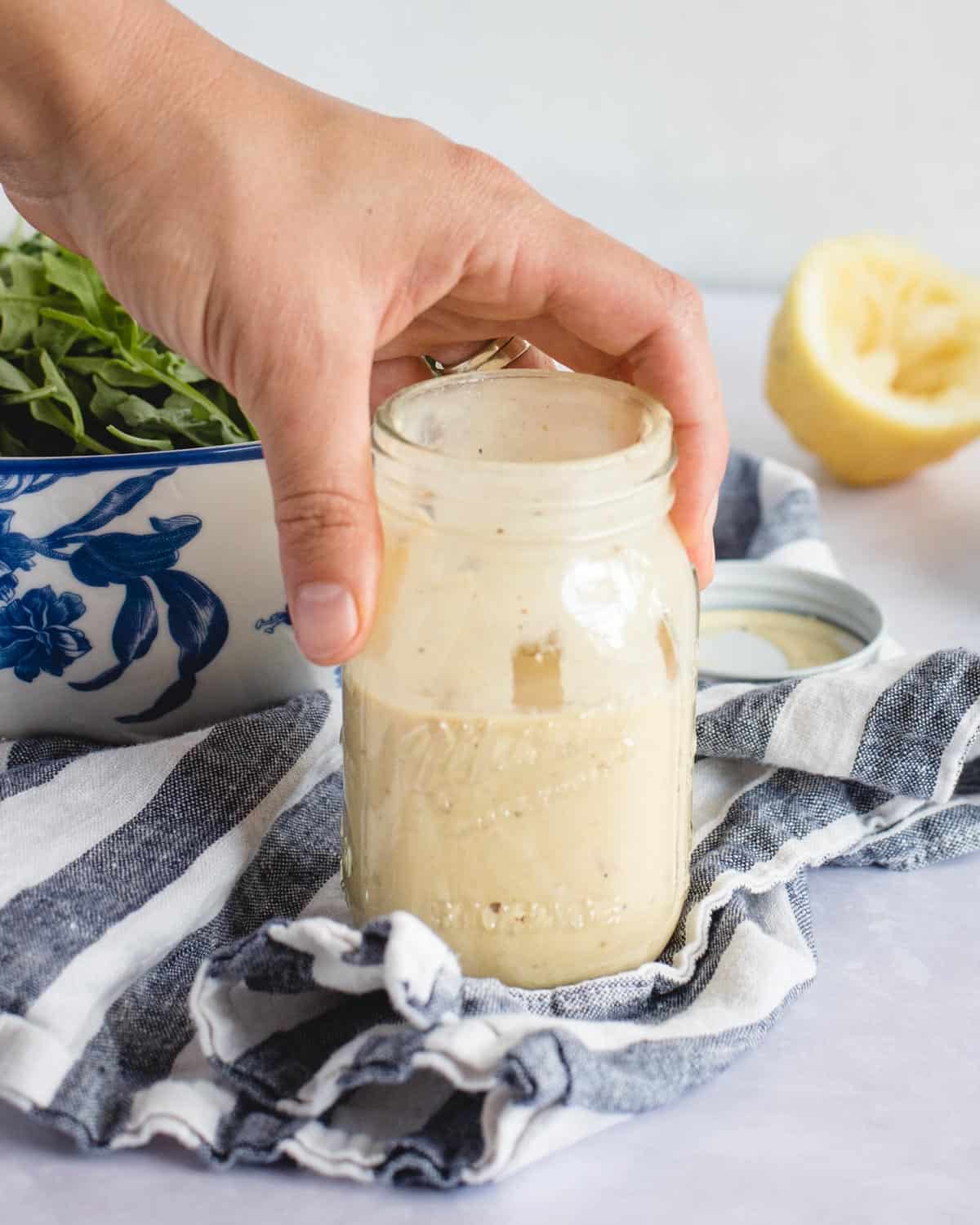 hand holding Mason jar of tahini dressing on a blue and white towel