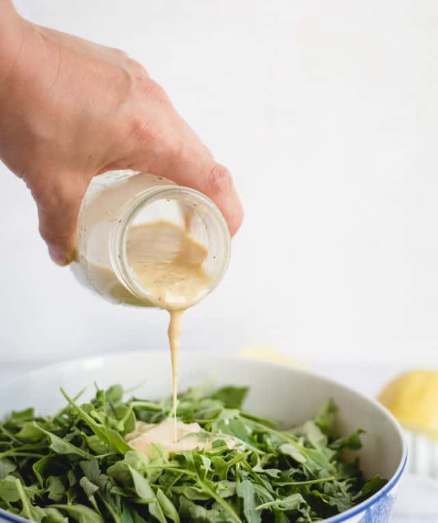 hand pouring lemon salad dressing over a green salad against a white background