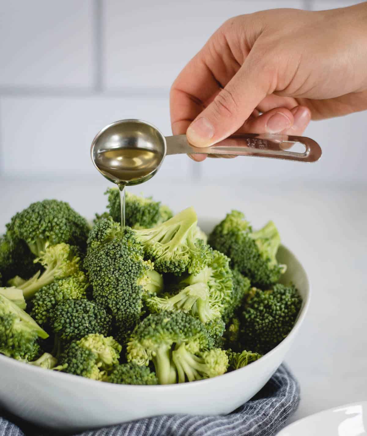 oil being poured onto a bowl of broccoli