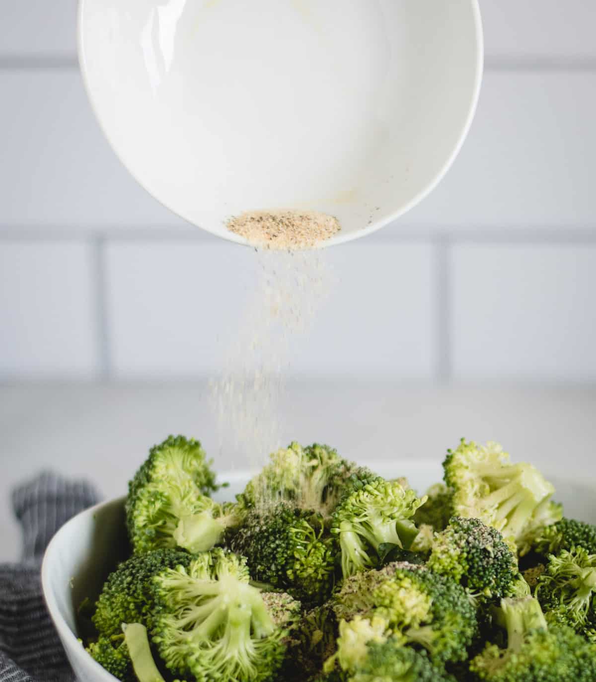 seasoning being sprinkled onto a bowl of broccoli