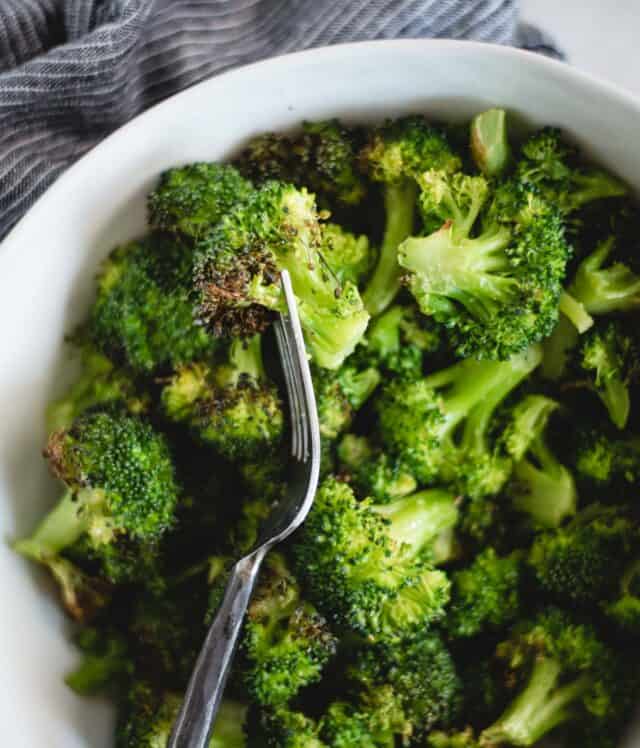 close up overhead picture of a fork stabbing a piece of broccoli out of a white bowl