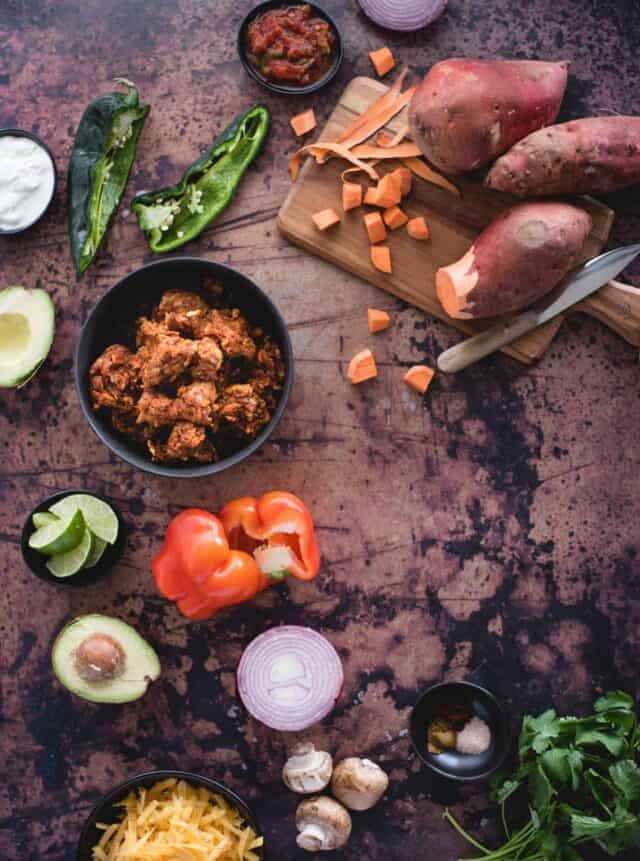 sweet potatoes, peppers, chorizo, and other ingredients needed to make a sweet potato skillet laid out on dark background