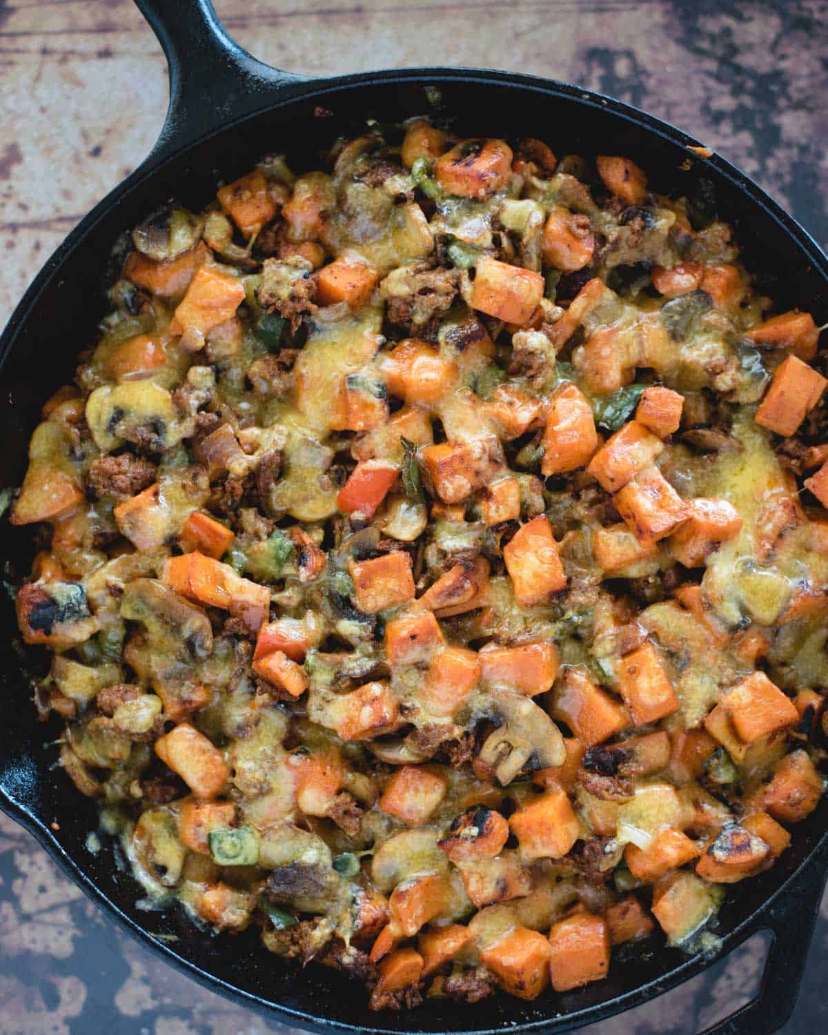 cheese melted onto a skillet of sweet potato, sausage and other veggies