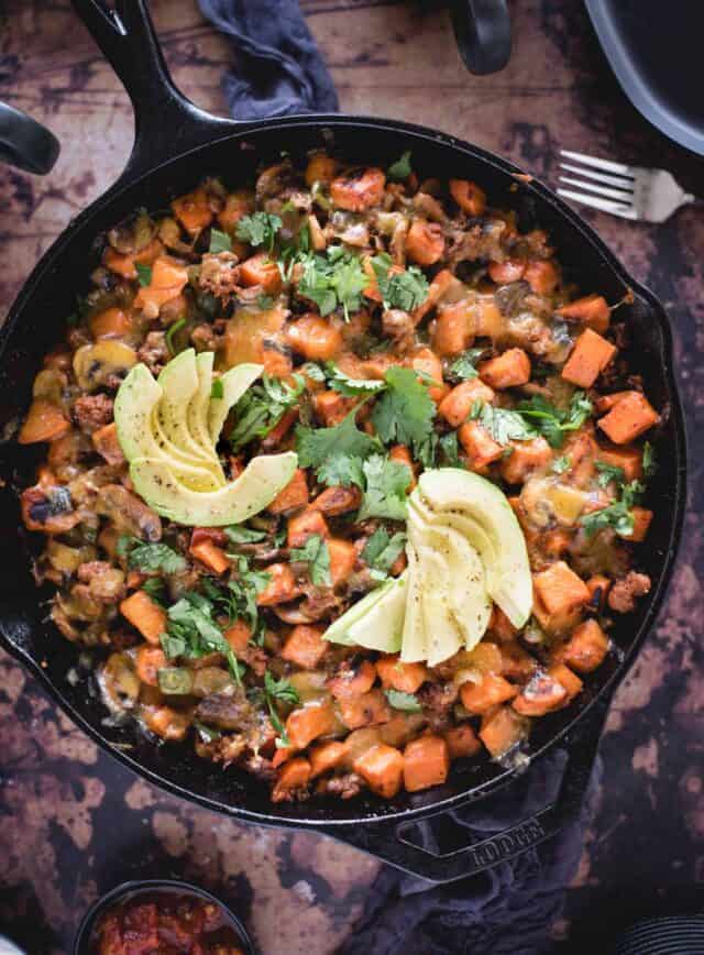 overhead close up picture of cheesy sweet potato skillet with avocado on top 
