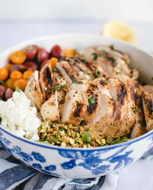 close up picture of green salad with grilled chicken on top, pistachios, tomatoes, and feta