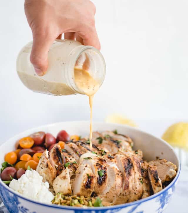 Hand pouring lemon dressing over a salad with sliced, grilled chicken on top