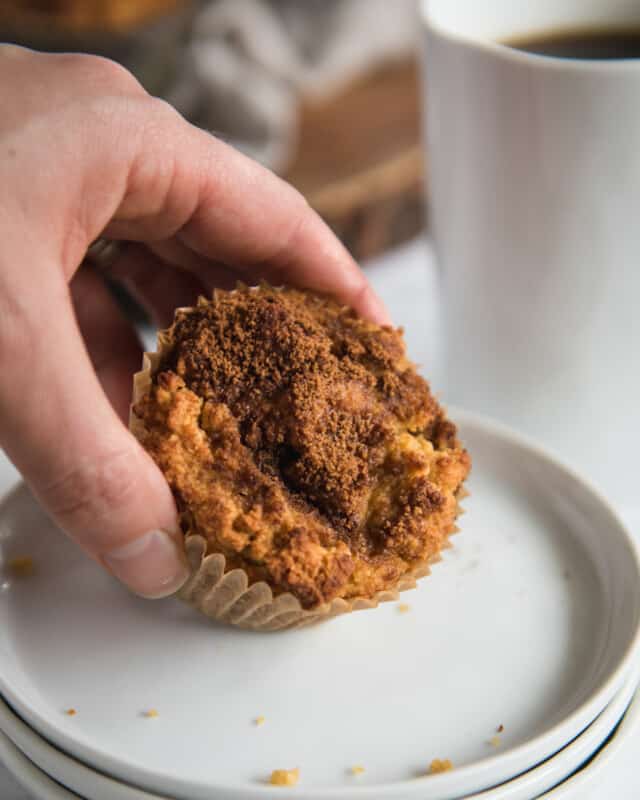 close up picture of hand grabbing coffee cake muffin with cinnamon sugar topping