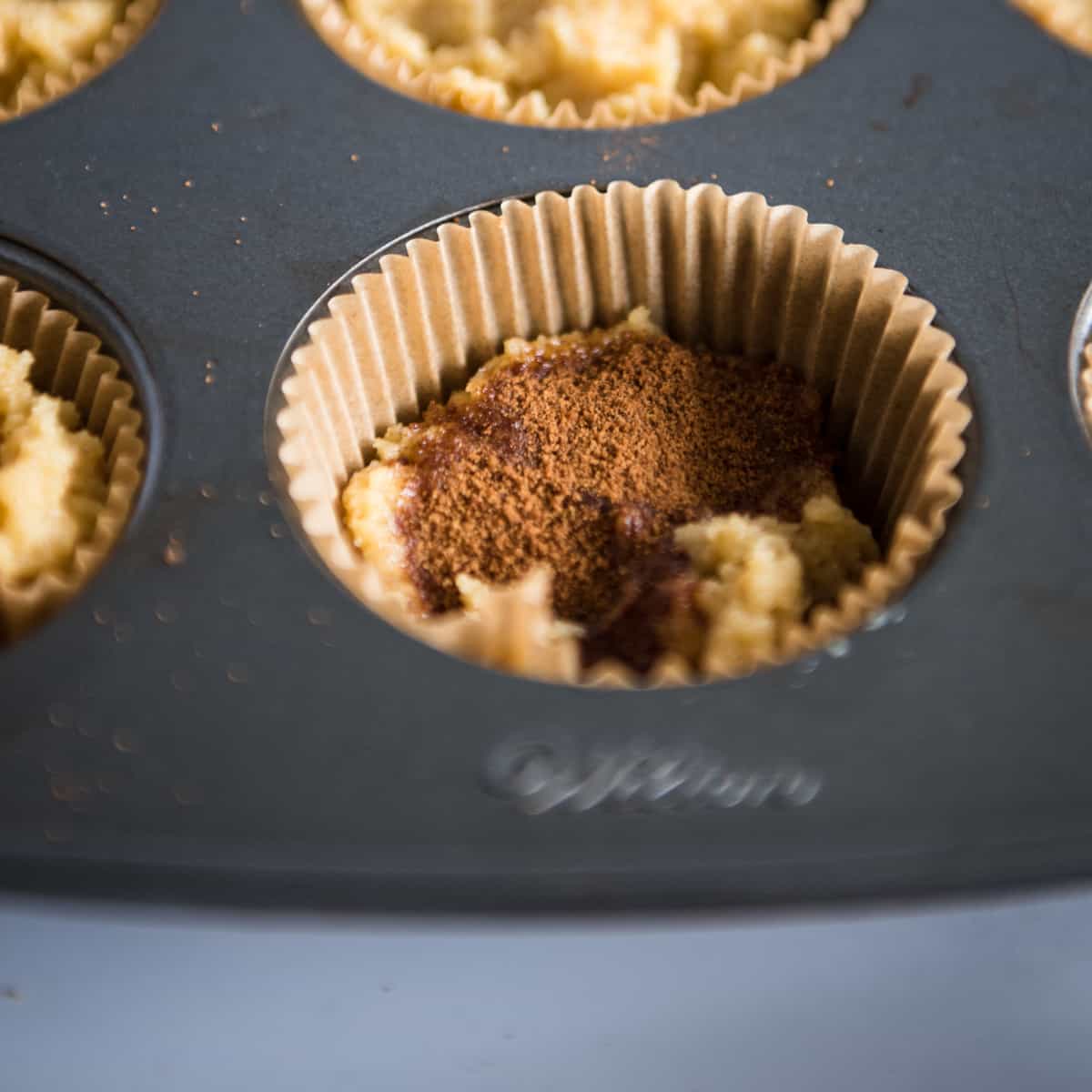 Muffin tin with cinnamon sugar sprinkled on top of muffin batter