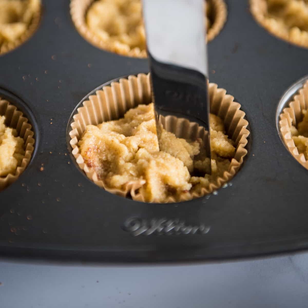 butter knife inserted into muffin tin swirling batter and cinnamon sugar together