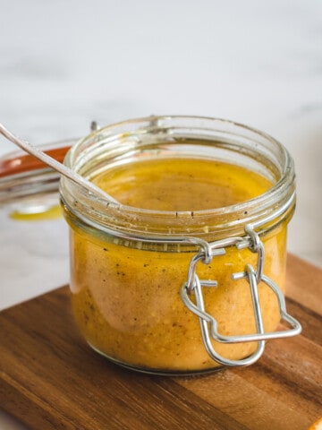 Close up picture of a jar of orange salad dressing on a cutting board