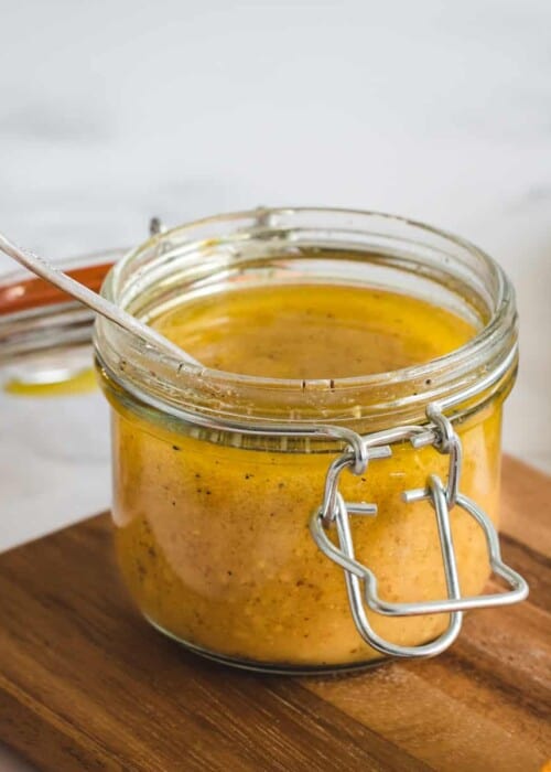 Close up picture of a jar of orange salad dressing on a cutting board