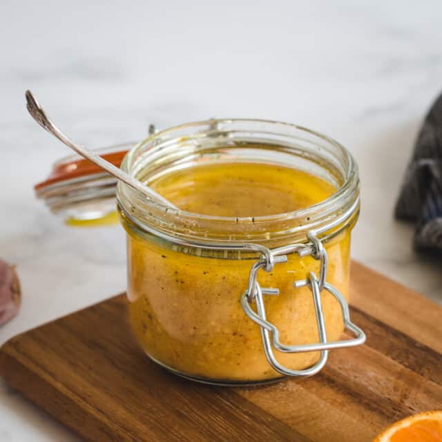 Close up picture of small canning jar of orange vinaigrette on a wood cutting board 