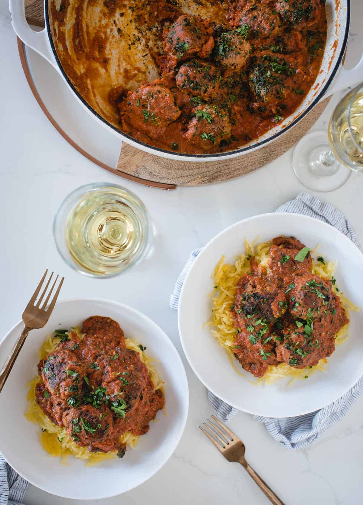 overhead picture of a pan of meatballs in sauce, 2 glasses of wine and two plated servings over pasta