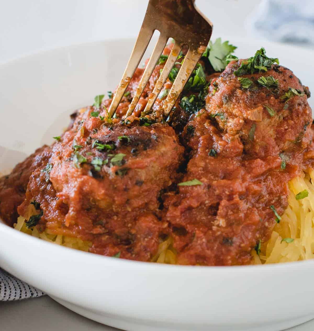 Close up picture of fork stabbed into bison meatball in red sauce on top of spaghetti 
