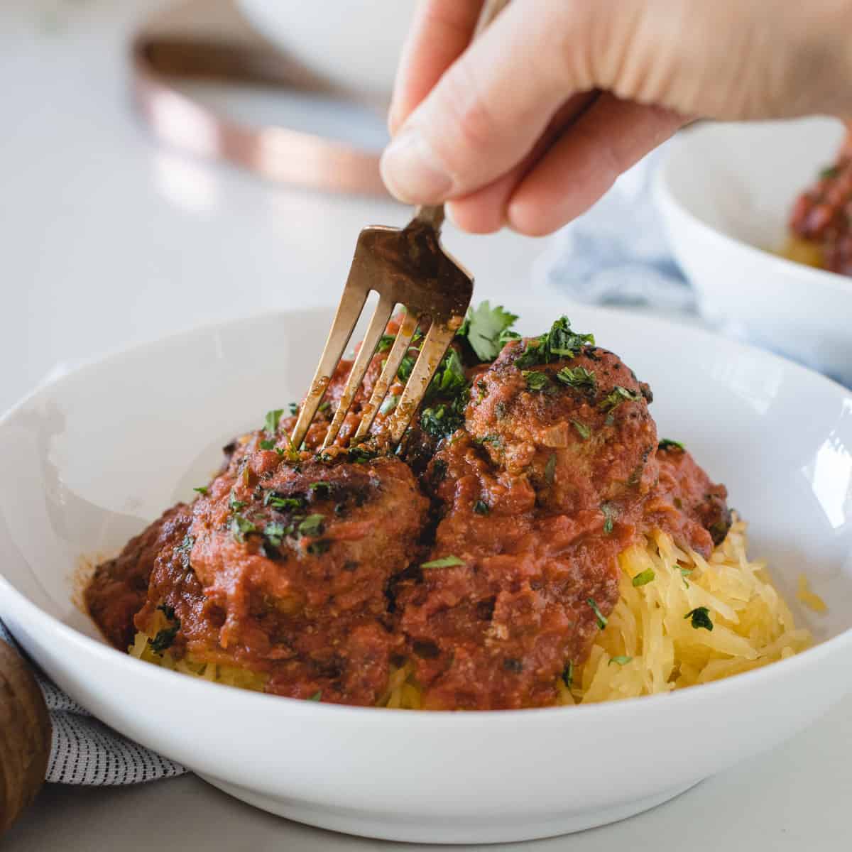 hand holding a fork stabbing into a bison meatball covered in red sauce in a white bowl